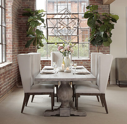 Grey wash trestle dining table with white wing chairs in room with brick wall