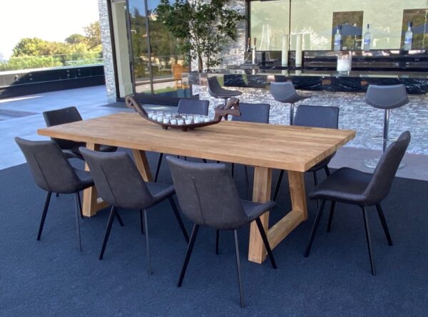 Large teak outdoor dining table shown with chairs and blue rug
