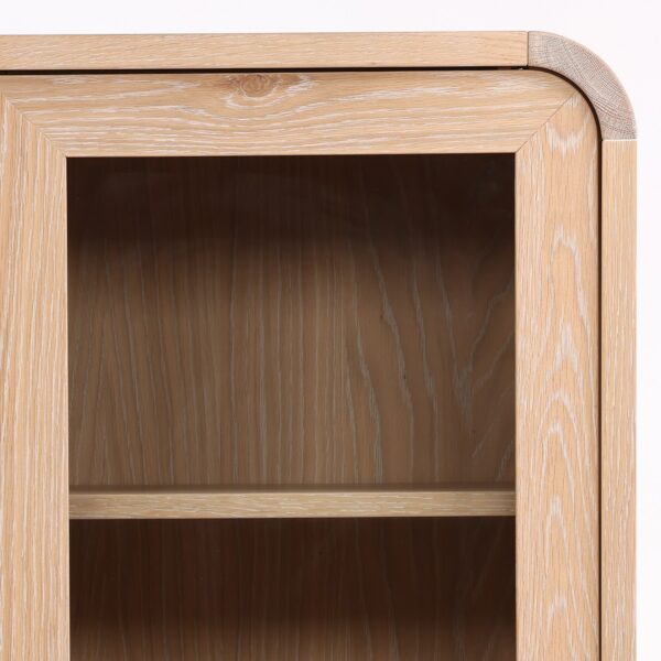 Tall cabinet with glass doors and shelves. Natural light wood color, corner detail